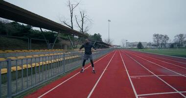 A man in a sports outfit with earphones in his ears does a warm-up standing at the stadium on a cold day - standing - in photo