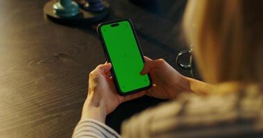 A woman uses a mobile phone with green screen sitting at a table indoors, close-up of her hands, an unrecognizable person - sitting photo