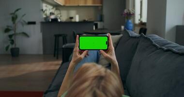 A woman holds a mobile phone with a green screen horizontally in her hands watching , rear view, an unrecognizable person - horizontally photo