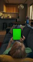 A woman uses a tablet with green screen lying on the couch at home, an unrecognizable person - tablet photo