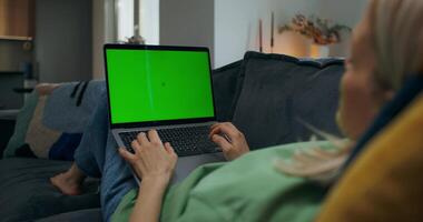 A woman uses a laptop with green screen lying on the couch at home, an unrecognizable person - unrecognizable photo