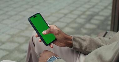 A man uses a mobile phone with a green screen sitting outdoors, close-up of his hands, an unrecognizable person - unrecognizable photo