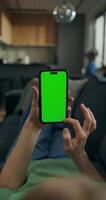 A woman uses a mobile phone with green screen lying on the couch at home. A rear view of her hands, an unrecognizable person photo
