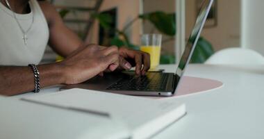 A man uses a laptop and writes in a notebook sitting at a table at home, close-up of his hand, an unrecognizable person - notebook photo