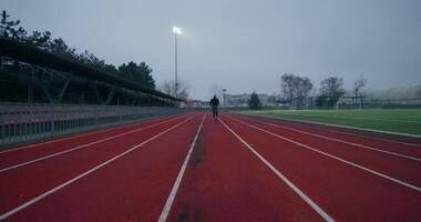 A man in sports clothes runs around the stadium on a cold day alone, front view - around photo