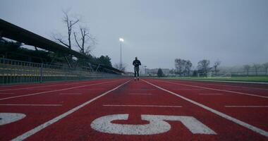 A man in sports clothes runs around the stadium on a cold day alone, front view photo