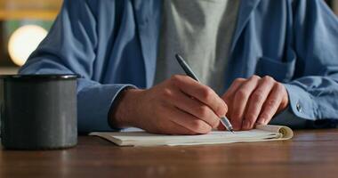 A man is writing in a notebook sitting at a table, close-up of his hands, an unrecognizable person - sitting photo
