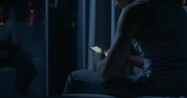 A man uses a mobile phone while sitting on the bed at night. Close-up of his hands, an unrecognizable person. Dark room, home interior photo