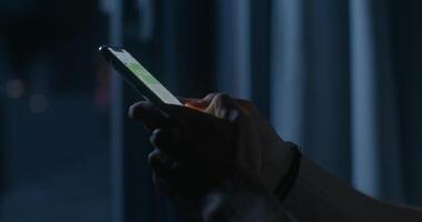A man uses a mobile phone while sitting on the bed at night. Close-up of his hands, an unrecognizable person. Dark room, home interior - mobile photo