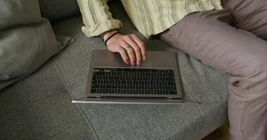 A bearded man uses a laptop and talks on a mobile phone sitting on the couch at home with a serious look. Daylight - mobile photo