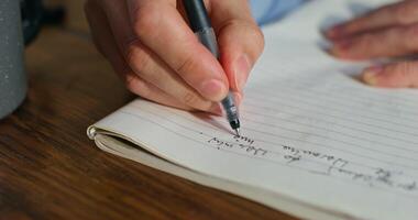A man is writing in a notebook sitting at a table, close-up of his hands, an unrecognizable person photo