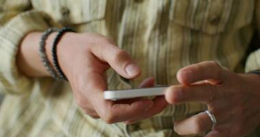 A man is typing on a mobile phone sitting on the couch at home. close-up of his hands, an unrecognizable person. Daylight photo