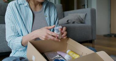 The woman opens the box and pulls out the cosmetics, she smiles. She is sitting on the floor near the sofa at home. Daylight - sitting photo