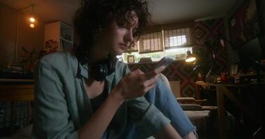 A young woman uses a mobile phone while sitting on a bed at home with a depressed look - depressed - woman photo