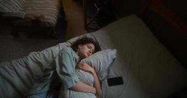 A woman is crying and hugging a pillow lying in bed at home. The mascara is smeared under the eyes. The mobile phone is on her bed photo