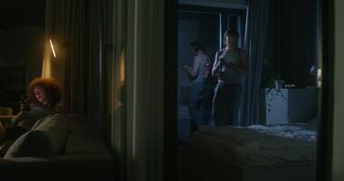 A woman uses a mobile phone sitting on the couch at home. The man throws the phone on the bed and lies down. He's upset. Home interior, night photo