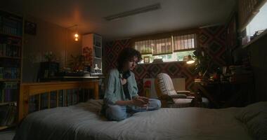 A young woman uses a mobile phone while sitting on a bed at home with a depressed look - sitting photo