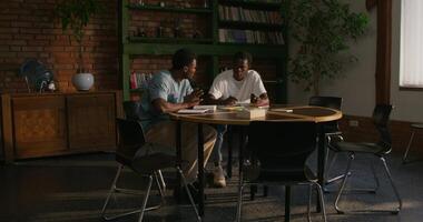 Two men are talking while studying the Bible together. They are sitting at the table indoors - talking photo
