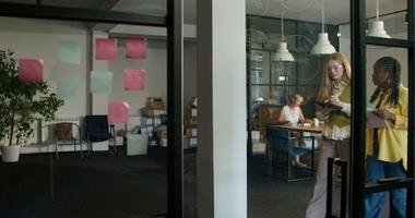 General view of a modern office. Empty boxes are lying near the wall. Two women are talking as they pass by. Daylight photo