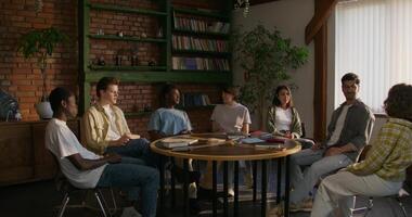 Bible Study Group. Young people talk in pairs while sitting at a table indoors. The books are on the table. Daylight photo