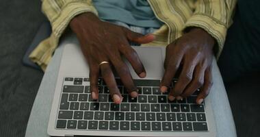 A man uses a laptop while sitting on the couch at home, close-up of his hands, an unrecognizable person. Daylight - unrecognizable photo