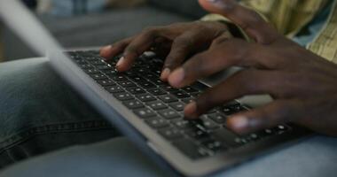 A man uses a laptop while sitting on the couch at home, close-up of his hands, an unrecognizable person. Daylight photo