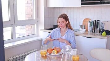 Close up of woman taking picture of her breakfast, selfie with croissant and sharing on social media at kitchen table at home in the morning video