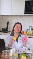 A nutritionist looking at the camera at a table with fruits and vegetables. Consultation on healthy eating using a donut and an apple as an example. video