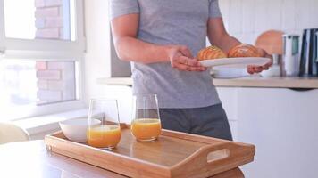 A man serves breakfast with croissants and orange juice for two on a tray in the kitchen. Breakfast in bed video