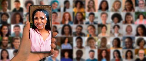 A person holds a smartphone showing a facial recognition display. Behind, a collage of diverse faces reflects the advanced technology in identification. photo