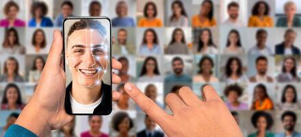 A person holds a smartphone displaying face recognition technology. The screen shows a smiling face with a digital overlay. Many portraits fill the background, highlighting diverse individuals. photo