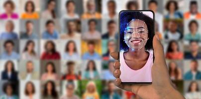 A smartphone is held in hand, showcasing a facial recognition scan of a smiling person. The background features a collage of diverse faces. This highlights the advanced technology in modern devices. photo