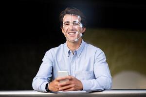 A young man smiles while holding a smartphone. Advanced facial recognition technology is analyzing his face, showcasing how identification checks are becoming part of daily life. photo