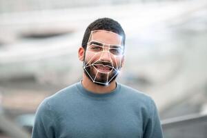 A man stands smiling outdoors while facial recognition technology analyzes his features. This reflects the new normal of identification processes in various settings. photo