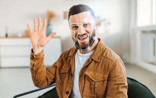 A man waves while sitting in a contemporary office, showcasing facial recognition technology. The room is bright and minimalistic, reflecting a modern approach to identification. photo