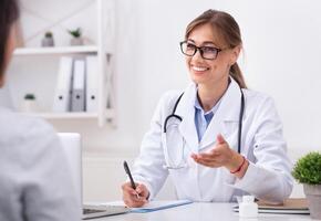Phisician's Visit. Cheerful Lady Doctor Talking With Unrecognizable Patient During Appointment Sitting In Office photo