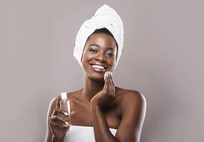 Young beautiful african woman cleaning her face from makeup with cotton pads and micellar water over gray background with copy space photo