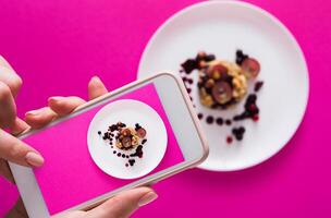Top view close-up of female hands making flat lay food photo with phone for restaurant menu or social network. Oatmeal porridge on pink background, mockup, template, copy space, shallow depth of field