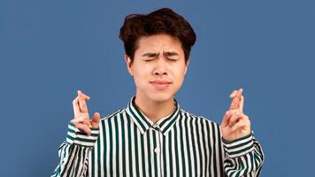 Cherished Wish. Superstitious Asian Man With Closed Eyes Crossing Fingers And Begging For Luck, Praying For Miracle, Hoping For Good Things To Happen, Isolated On Purple Studio Background, Copy Space photo