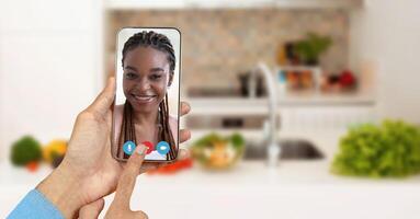 A person is enjoying a call on a smartphone from their kitchen. The screen shows a smiling individual, highlighting the connection made through online communication. photo