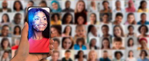 A hand holds a smartphone displaying a facial recognition feature. Behind, a diverse collage of faces shows various expressions and identities, symbolizing modern identification technology. photo