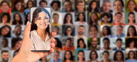 A hand holds a smartphone displaying facial recognition technology. The device scans a person's face against a collage of diverse portraits, showcasing modern identification methods in action. photo