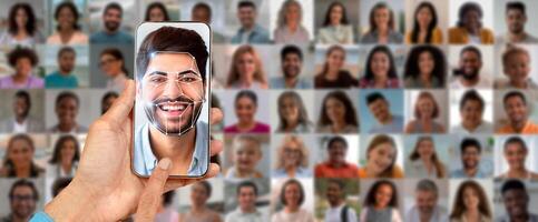 A person holds a smartphone displaying face recognition technology while scanning their own image. The background features a collage of diverse faces, representing modern identification methods. photo