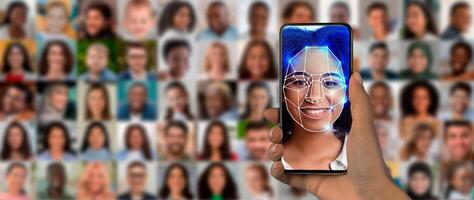 A hand holds a smartphone displaying a digital face scan. Surrounding the phone, a collage of diverse portraits highlights the technology's use in identity verification. photo