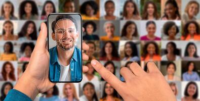 A hand holds a smartphone displaying a facial recognition scan. Behind, a collage of diverse faces highlights contemporary technology's role in identification and security practices. photo