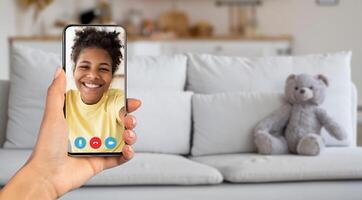 A person smiles while enjoying a call on a smartphone. The cozy living room features a soft couch and a teddy bear, creating a warm environment for communication. photo