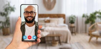 A person enjoys a call with a smiling individual on their smartphone, showcasing a comfortable home environment filled with plants and cozy decor. photo