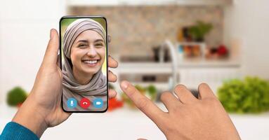 A person smiles while engaging in a call on their smartphone, showcasing a friendly interaction. The cozy kitchen background adds warmth to the conversation. photo