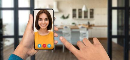 A person is holding a smartphone to engage in a lively call while in their cozy home. The background features a well-lit kitchen setting, enhancing the atmosphere of connection. photo