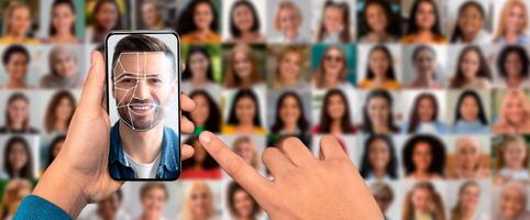 A hand holding a smartphone displays facial recognition technology with a smiling face on the screen. In the background, a collage of various portraits showcases the face identification process. photo